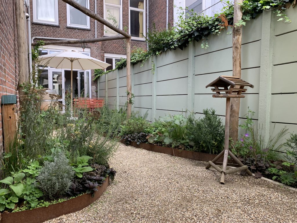 Uitzicht vanuit het beschutte zitje op het huis en de groene beplanting